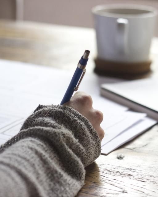 Mão escrevendo num caderno ao lado de uma xícara de café