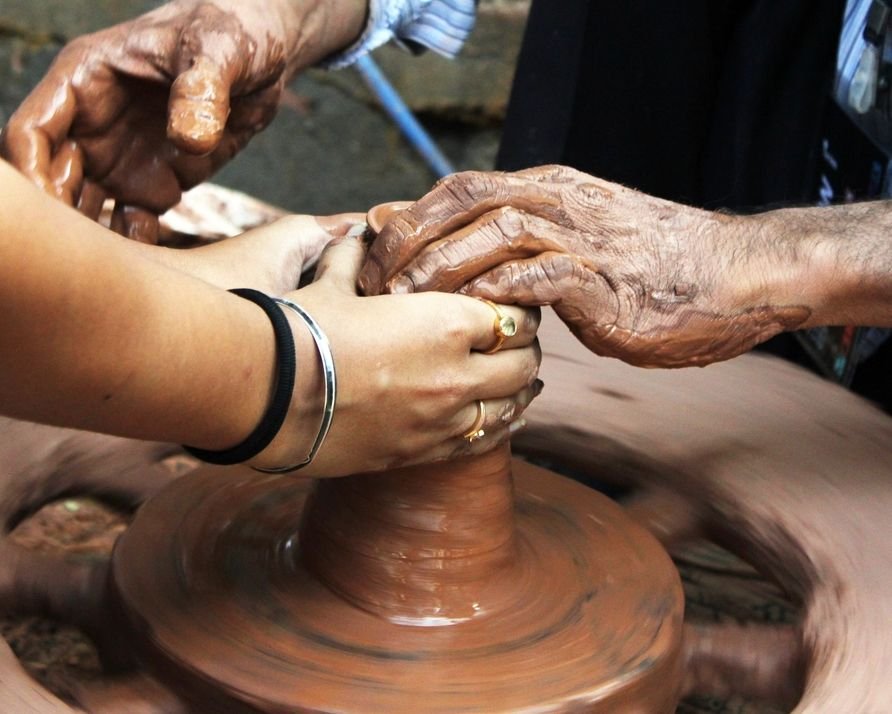 Mãos de duas gerações moldando barro no torno