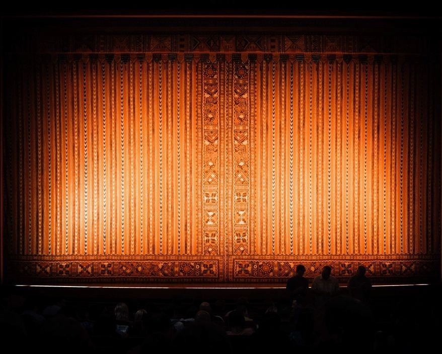 Cortina de teatro iluminada e plateia em silhueta